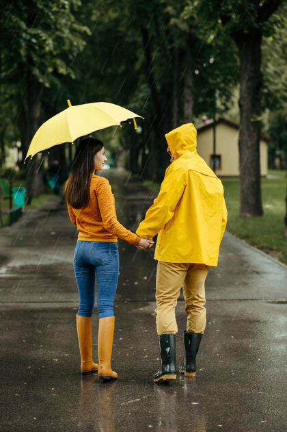 一对雨天 一对恋人撑着伞在公园散步戴曼穿着胶靴的女人走在小路上 小巷里天气潮湿自然女性男朋友