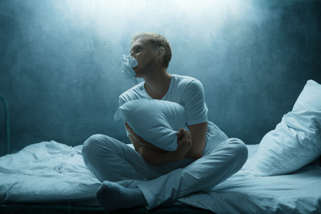 人精神病男人在床上抱枕 失眠恐怖 黑暗的房间…迷幻剂男人每晚都有问题 抑郁和压力 悲伤 精神病院脸人概念