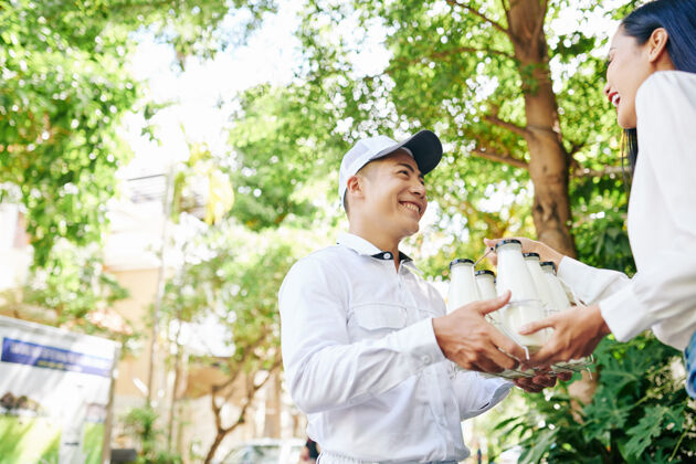 盒子快乐微笑的越南送货员给漂亮的年轻女子一套奶瓶新鲜接收男