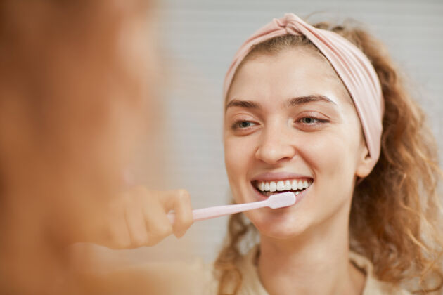 镜子年轻女子微笑着在前面 而清洁她的牙齿在早上牙齿微笑室内家庭浴室