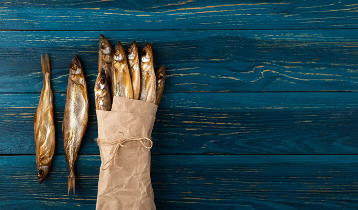 餐鱼干是一种理想的小吃啤酒包装好的在深蓝色木制背景上的旧工艺纸上干咸味冷