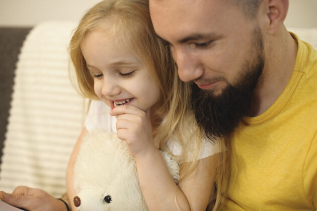 小玩意一个可爱的金发小女孩的特写照片 在妈妈上班的时候 她和爸爸在家看书 微笑着父母小胡子