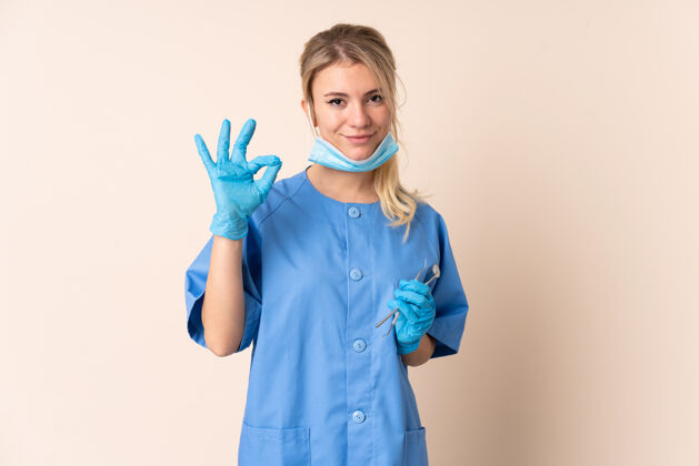年轻人一名女牙医拿着工具在隔离的背景下用手指显示ok标志医学医生女孩