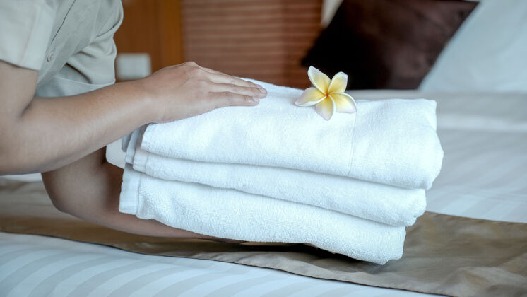 毛巾酒店女佣的手把鸡蛋花和毛巾放在豪华酒店房间的床上 为游客旅行做好准备客房服务女服务员
