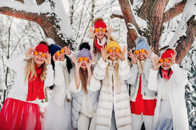 帽子冬天站着一大群带橘子的姑娘森林女孩穿着红白相间的衣服 在白雪覆盖的森林里结着水果节日衣服风景