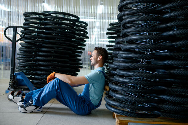 轮胎一名男工人站在一个托盘上的自行车车轮堆上工厂自行车轮圈车间流水线 轮圈零件安装 现代工艺人零件运动