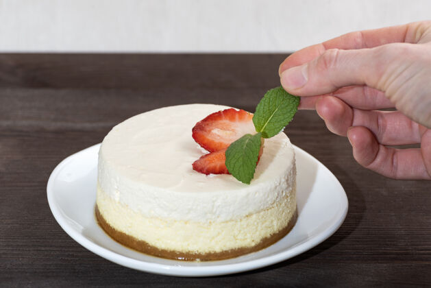 装饰芝士蛋糕配新鲜草莓 白色盘子女人手工装饰的蛋糕是薄荷糖美味美味新鲜