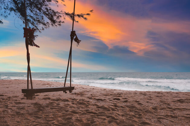波浪夕阳下的沙滩上 五彩缤纷的天空中 木制秋千的剪影沙滩风景海滩