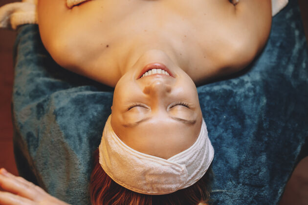 过程俯视图 一位美丽的年轻女子靠在水疗床上 闭着眼睛放松 同时在一家健康水疗沙龙做皮肤护理程序按摩平滑肖像