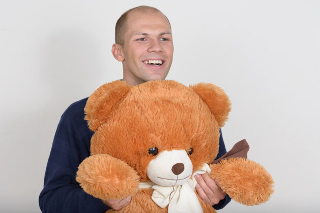 射击快乐的年轻英俊的秃头男子手持大泰迪熊的画像大熊爱