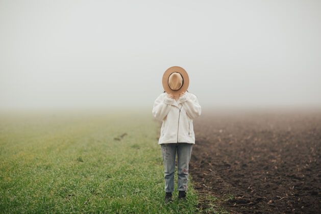 田野戴着帽子的女孩站在绿草如茵的草地和大地上白天雾女人
