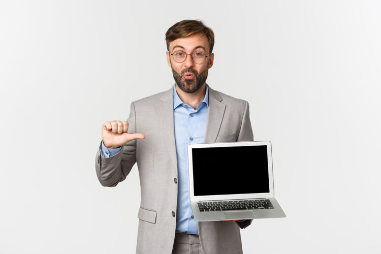 帅气戴着眼镜 穿着灰色西装 留着幸福胡须的商人的画像 指着笔记本电脑表演科技微笑