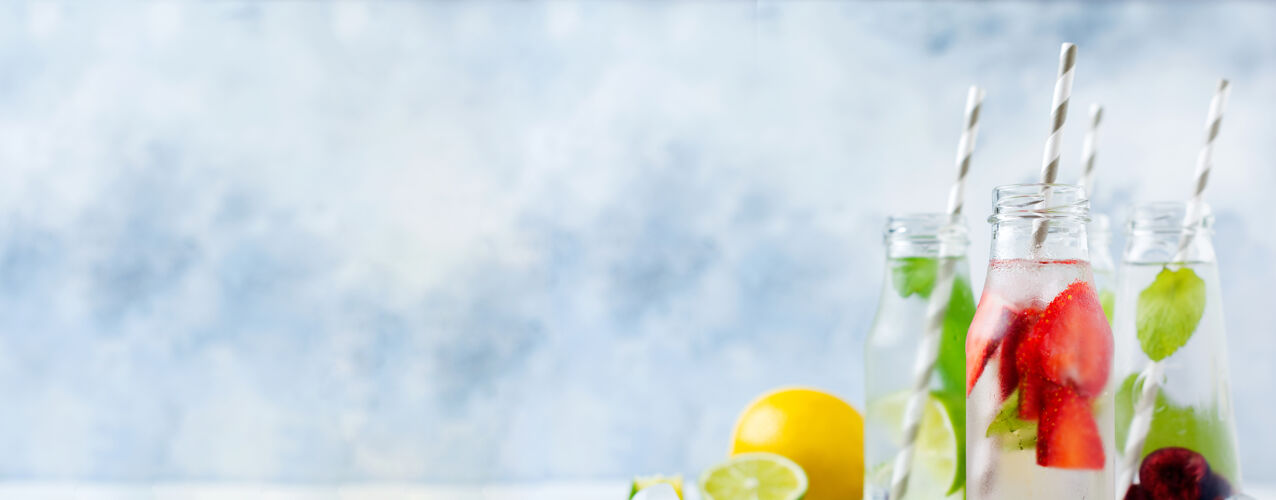 自制瓶装柠檬水清新夏季柠檬水与石灰 草莓 樱桃 黄瓜和冰在灰色的混凝土表面冰排毒玻璃