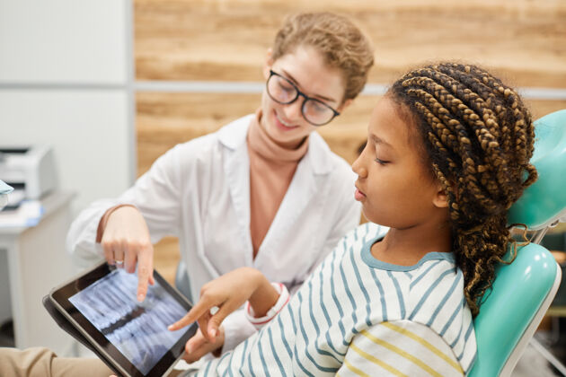 数字平板电脑小女孩坐在椅子上 和牙科诊所的牙医一起看牙齿的x光照片女孩电脑看