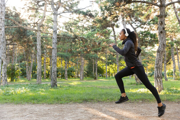 女运动员图为20多岁的健身女士穿着黑色运动服 戴着耳机 一边在绿色公园跑步成人年轻跑步