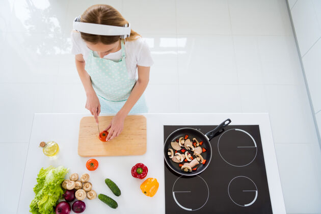 晚餐家庭主妇早上听音乐的高角度照片现代耳机为素食沙拉切西红柿站在白色厨房室内印章耳机听