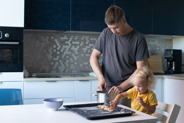 自制年轻的父亲和他漂亮的小女儿在做饭一起一家人在厨房里开心地做饼干厨房女孩金发卷发配料团聚休闲