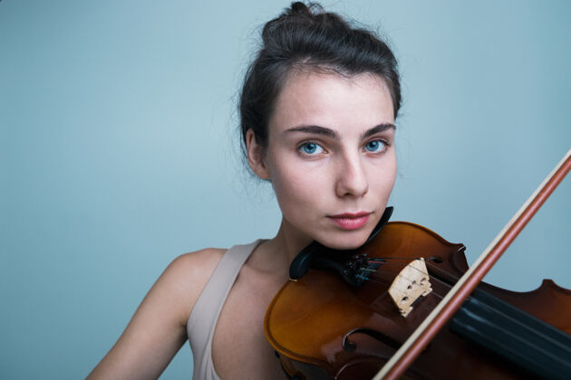 弦乐一个美丽的年轻女子与蓝色背景上孤立的小提琴合影的特写肖像年轻人肖像经典