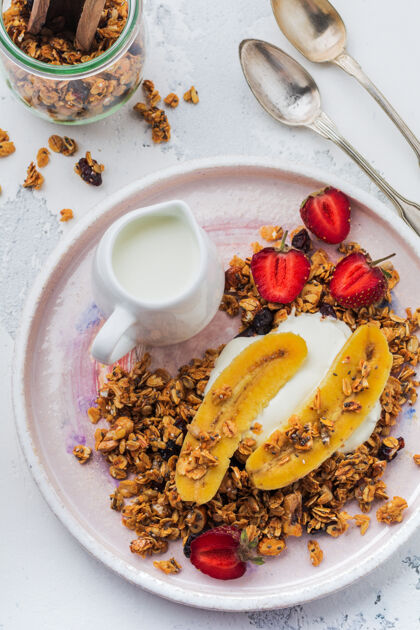 坚果燕麦格兰诺拉麦片配酸奶 新鲜草莓和香蕉 芝麻籽 向日葵和蜂蜜 用白色陶瓷盘放在浅色表面奶油种子水果