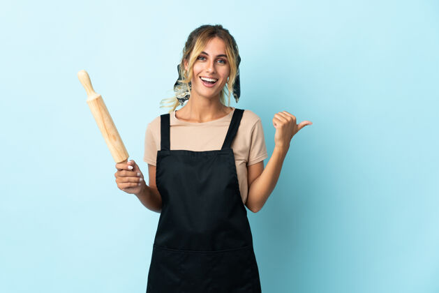 别针年轻的金发乌拉圭厨娘孤零零地指着蓝色的边上呈现一款产品成人工作厨房
