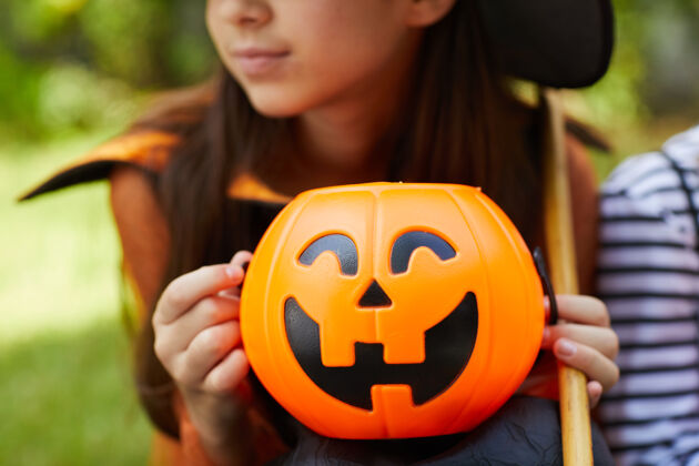 季节特写镜头中的小女孩在女巫服装举行玩具南瓜在她的手 而坐在户外十月不给糖就捣蛋天