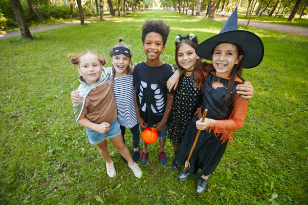 童年穿着万圣节服装的快乐孩子们站在公园里互相拥抱 对着镜头微笑的画像享受十月帽子