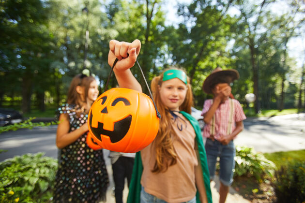 后代照片中的女孩拿着一个装着糖果的南瓜袋 和她的朋友们站在户外日子聚会小学