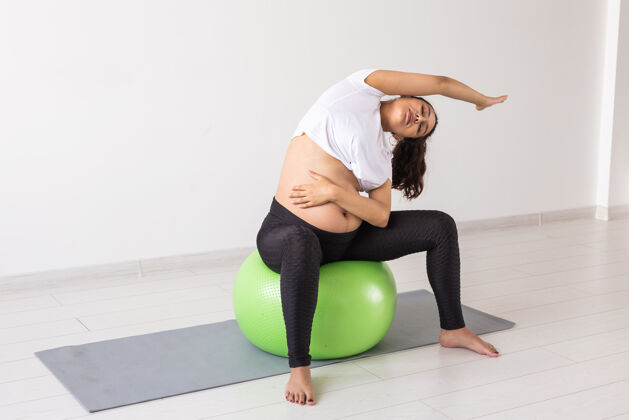 姿势年轻灵活的孕妇用健身球做体操简单放松胃