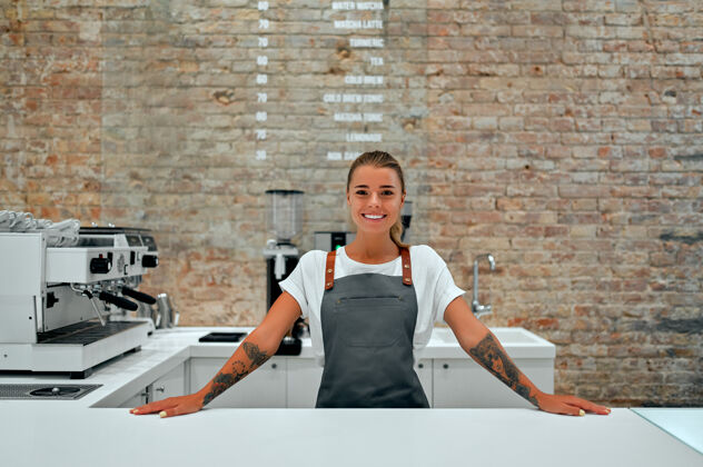 职业年轻的女咖啡师站在咖啡店的柜台前微笑着咖啡师围裙热
