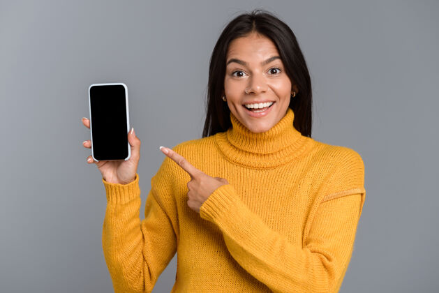 广告一个快乐随意的年轻女子的肖像被隔离在灰色的墙上 手机屏幕显示空白空白人女性