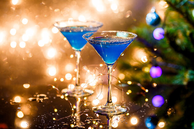 庆典圣诞照片的两个酒杯蓝色鸡尾酒和花环上模糊的蓝色新年新年味道季节