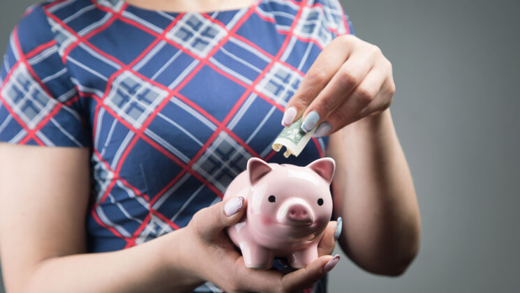 女性一个穿着裙子的女人把一美元扔进了一个存钱罐储蓄猪人