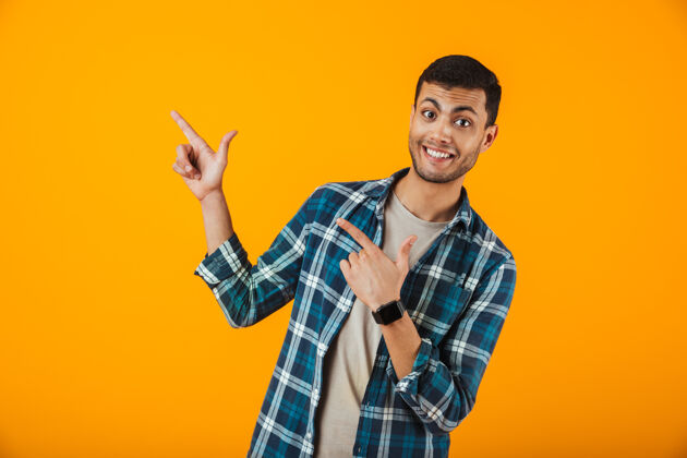 男性一个穿着格子衬衫的快乐的年轻人孤零零地站在橙色的墙上 把手指移开欢呼年轻人