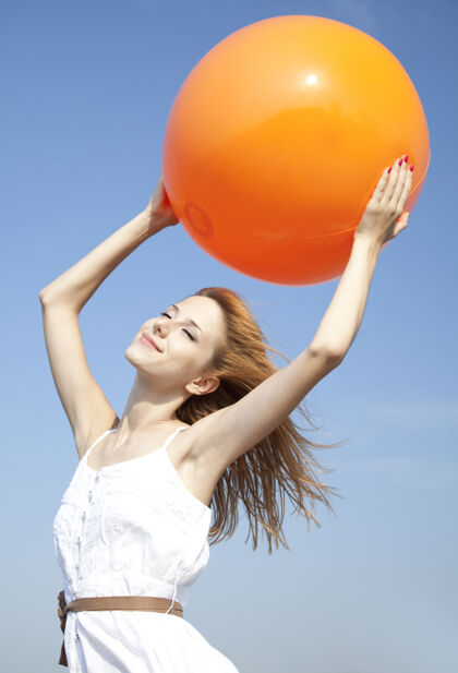 橙色红发女孩拿着球在蓝天上蓝色天空外面