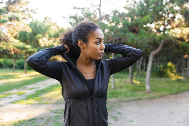 跑步20多岁的可爱女人穿着黑色运动服 穿过绿色公园精力充沛身体健身