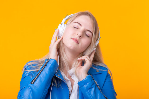 爱可爱积极的年轻金发女孩的肖像 戴着耳机 穿着蓝色夹克 听着最喜欢的音乐朋友成人学校