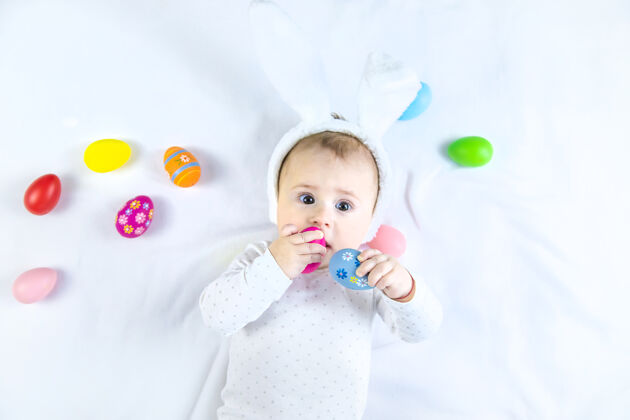 孩子宝宝穿得像兔子 在白色的表面上放复活节彩蛋节日小花式