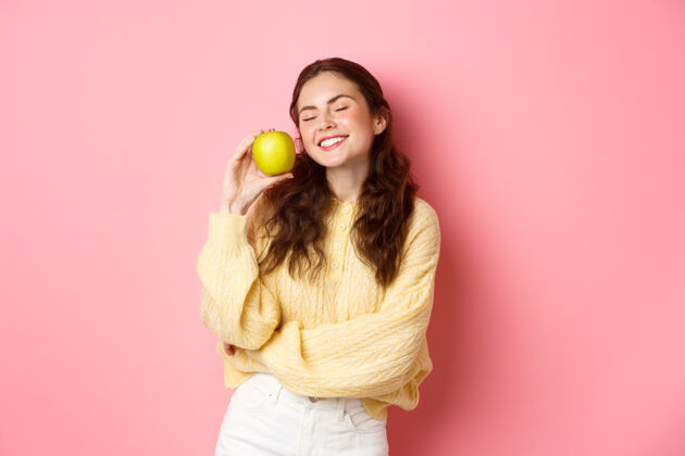 候选人健康 口腔和人的概念快乐女孩展示她洁白完美的牙齿 微笑和绿色的苹果 吃健康的食物和水果 站在粉红色的墙上休闲女性情绪