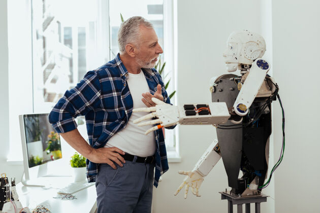 建筑智能技术严肃的老人一边看着机器人一边和它交谈开发成熟人