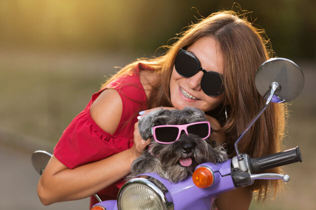 道路戴着墨镜的小狗 坐在丁香色的轻便摩托车上的快乐女孩 概念小狗狗摩托车