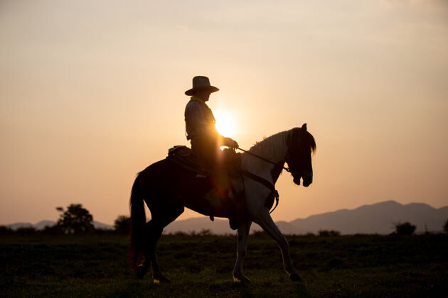 头盔牛仔骑在马背上迎着美丽的日落阳光马日落
