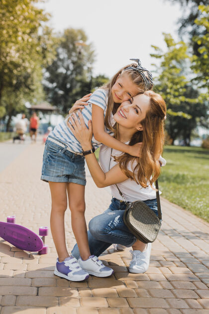 环境小女孩体贴的年轻漂亮的妈妈抱着她的小女孩穿着时髦的牛仔裤短裤家庭小休息
