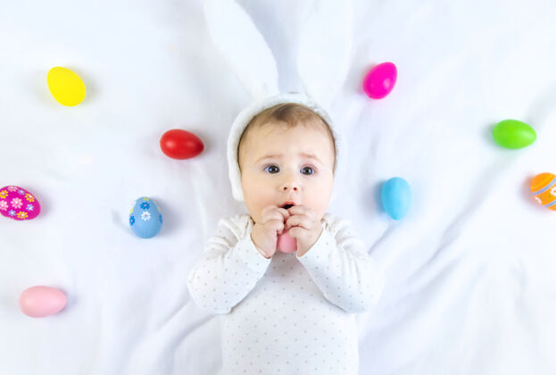 小宝宝穿得像兔子 在白色的表面上放复活节彩蛋小有趣年轻