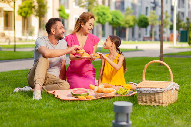 为人父母美味的食物快乐的爸爸和女儿微笑着从盘子里拿汉堡包男性男人女孩