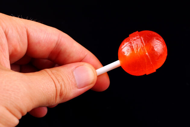 棒棒糖手里拿着红糖 粘在黑色的表面上公平棒颜色