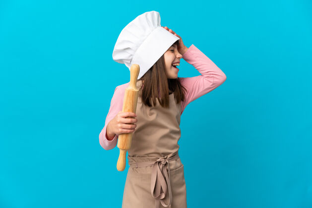 厨房抱着擀面杖的小女孩孤零零地站在蓝色的墙上 满脸笑容肖像模型骄傲