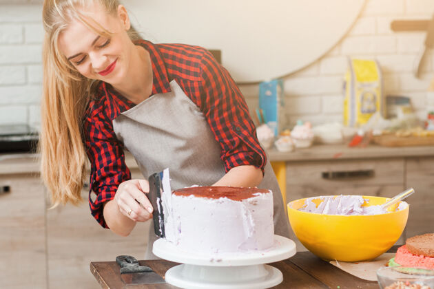 处理年轻可爱的女人在木制的餐桌上用白色奶油做饼干蛋糕碗甜点烘焙