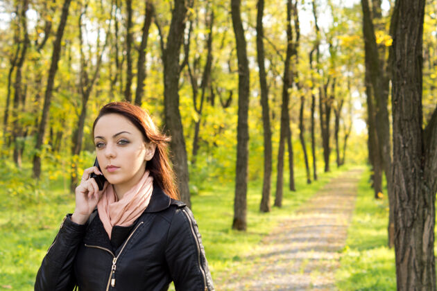 电话迷人的黑发女人走在公园的人行道上用手机聊天走道无线站