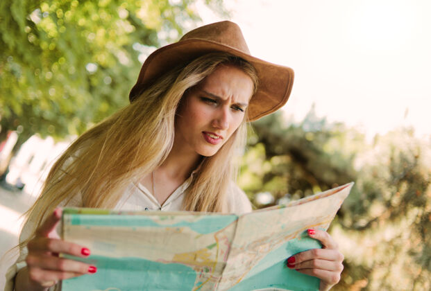 年轻一个戴毡帽的金发女人看着城市地图 走在一个陌生的户外城市困惑休闲成人