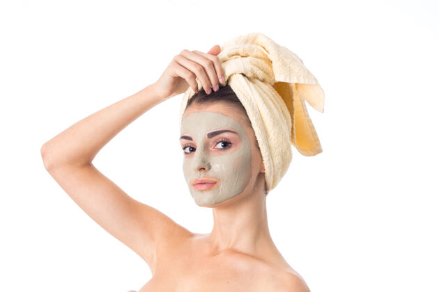 制造可爱的年轻女子用洁面面膜和毛巾在白色的墙上隔离在头上护理她的皮肤皮肤护理肖像年轻